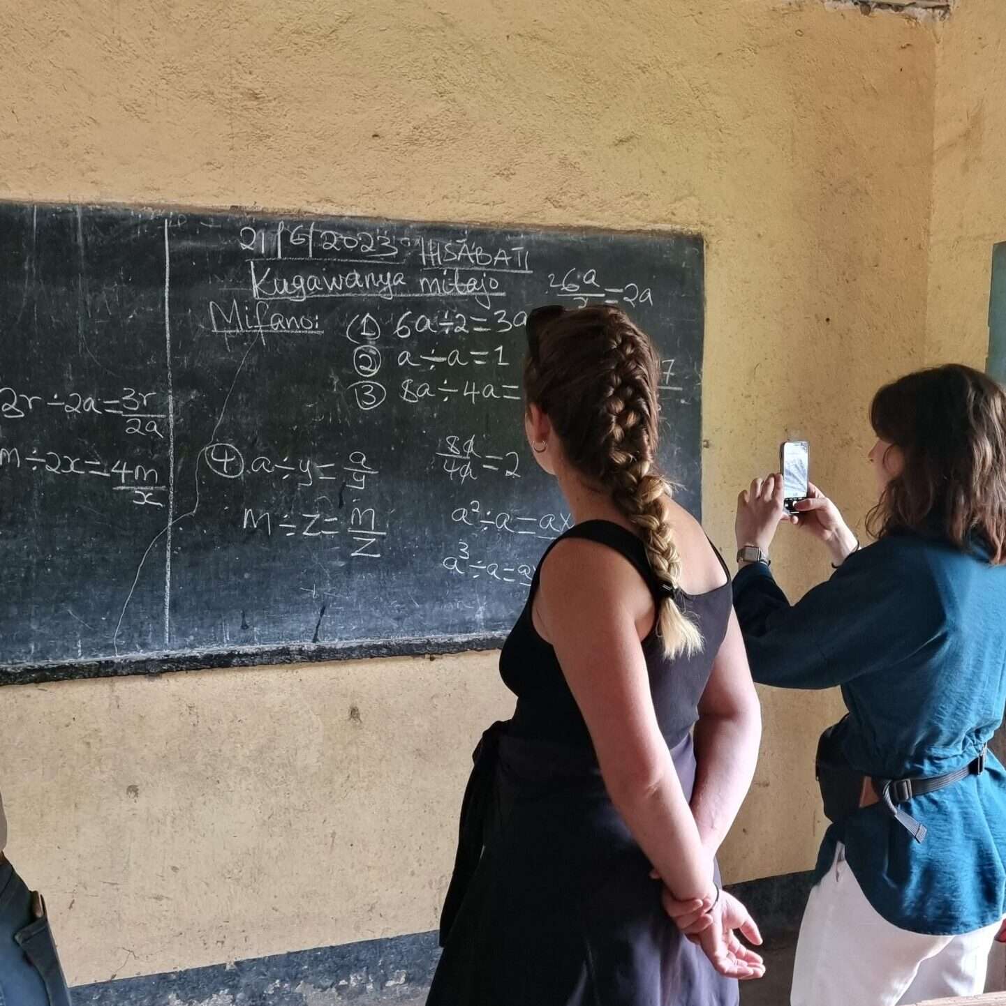 Tableau de l'école primaire avec un exercice de mathématique écrit à la craie. Deux élèves ostéopathes le prennent en photo.